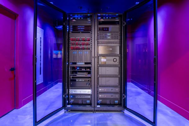 A stylish equipment rack with a variety of electronics housed in a glass-enclosed cabinet, illuminated by ambient purple lighting.